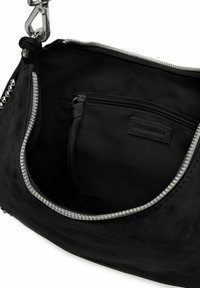 Intérieur d'un sac à main en daim noir avec fermeture éclair argentée, comportant une petite poche intérieure et une étiquette. Texture douce avec des accents matériels minimaux.