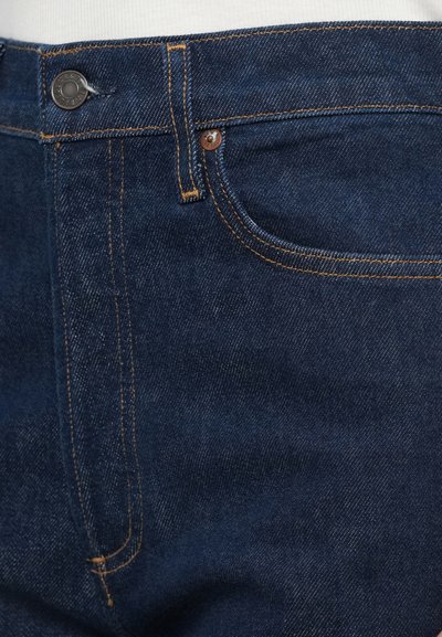 Tmavomodré rifle z denimu so sýto oranžovým prešívaním, s zapínaním na gombíky a predným vreckom. Hladká textúra s klasickým strihom.