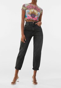 Zkrácený grafický tričko s barevným designem; vysoké černé džíny; čiré sandály na blokovém podpatku; hladká textura a přiléhavý silueta.