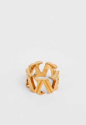 Gold metal ring featuring cut-out letters, rounded edges, and a smooth finish. The design is open, allowing light to pass through.