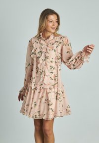 Abito floreale rosa chiaro realizzato in tessuto trasparente con dettagli arricciati, maniche lunghe a sbuffo e gonna a strati. Presenta una chiusura con bottoni.
