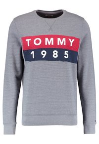 Sudadera gris con cuello redondo. Presenta un gráfico central en rojo, azul marino y blanco, que muestra "TOMMY 1985". Puños y dobladillo acanalados.