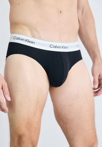 Fekete férfi alsónadrág szürke derékpánttal, amelyen fekete "Calvin Klein" logó található. Simább szövet és testhez simuló kialakítás.