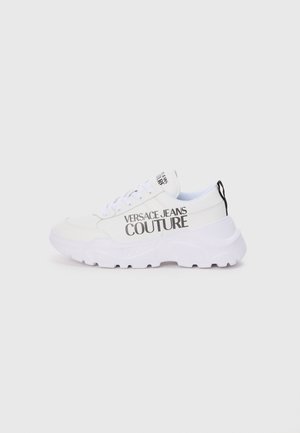 Baskets blanches avec une semelle épaisse, arborant le logo "VERSACE JEANS COUTURE" en noir. Matériau lisse, design à lacets et languette au talon.