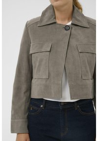 Pilka zomšinė trumpa striukė su dideliu atvartų apykakliu, priekyje sagomis užsegama ir dviem krūtinės kišenėmis. Dėvima ant baltos palaidinės ir tamsių džinsų.