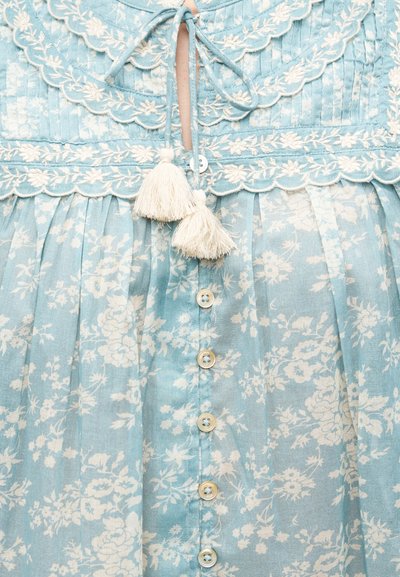 Φόρεμα ανοιχτού μπλε με λουλουδάτο σχέδιο και εκρού κεντήματα, με κυματιστές άκρες, κουμπιά μπροστά και δύο μεγάλες εκρού φούντες που κρέμονται από το κορδόνι στο ντεκολτέ.