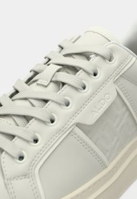 Lysegrå sneaker lavet af glat syntetisk materiale, med rundet tå, teksturerede detaljer, flade snørebånd og præget logodetalje.