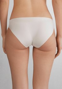 Weiße Bikini-Briefs aus glattem, dehnbarem Stoff, mit einem tief sitzenden Design und minimaler Abdeckung, die den Rücken betont. Nahtlose Verarbeitung für zusätzlichen Komfort.