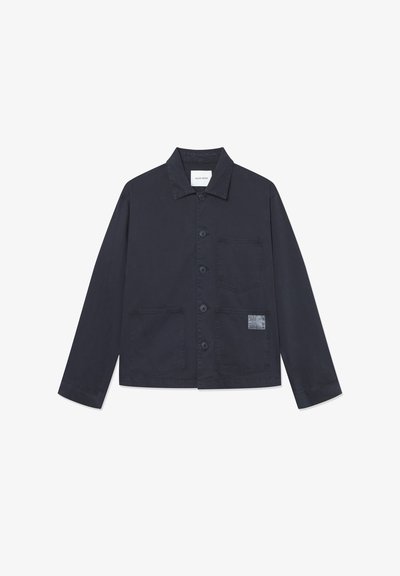 Tumši zila kokvilnas jaka ar apkakli, priekšējo pogu aizdari, divām lielām kabatām un struktūru apdari kreisajā kabatā.