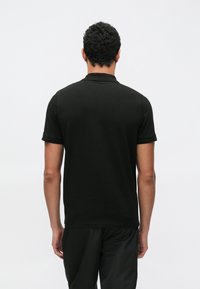 Čierne polo tričko s klasickým golierom, krátkymi rukávmi a hladkou textúrou látky, zobrazené zozadu na jednoduchom pozadí.