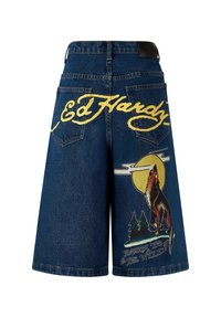 Tummansiniset farkkushortsit, joissa on väljät leikkaukset. Piirteet keltainen "Ed Hardy" -logo ja susigrafiikka kuu ja puut taustalla.