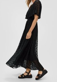 Černé maxi šaty s leopardím potiskem, průhlednými volánovými rukávy a elastickým pasem. Nosí se s tlustými černými platformovými sandály.