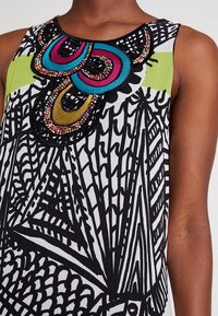 Vêtement sans manches avec motif géométrique abstrait noir et blanc et broderie perlée colorée en bleu, rose, jaune et multicolore au niveau de l'encolure.