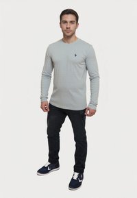 Világosszürke, hosszú ujjú póló texturált mintával, sötét farmernadrággal és fehér részletekkel ellátott kék sportcipővel párosítva.