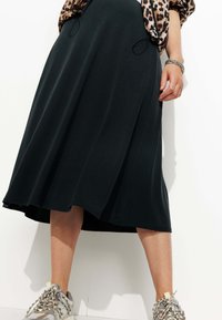 Jupe midi noire en tissu léger, avec une texture lisse et un design fluide. Associée à des baskets décontractées avec un motif de dentelle décoratif.