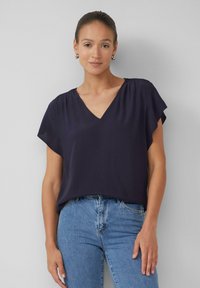 Blouse bleu marine avec un décolleté en V, des manches courtes évasées et un tissu doux. Associée à un jean en denim bleu clair. Design simple sans motifs.