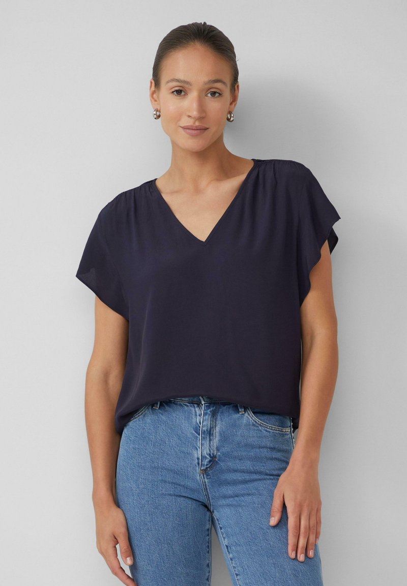 Blouse bleu marine avec un décolleté en V, des manches courtes évasées et un tissu doux. Associée à un jean en denim bleu clair. Design simple sans motifs.