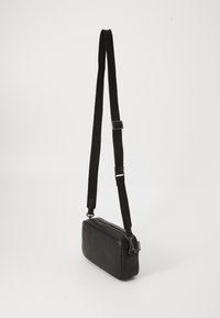 Black shoulder bag with a rectangular shape, made of textured material. Features an adjustable black strap and a zip closure.