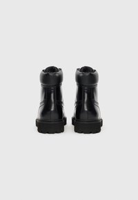 Bottes de cheville en cuir noir avec un bout rond, un col rembourré et une semelle en caoutchouc texturée dotée de rainures profondes pour une meilleure traction.