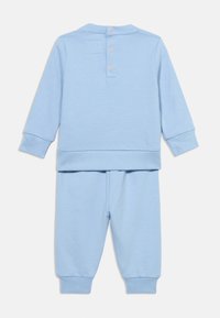 Σετ φόρμας ανοικτού γαλάζιου χρώματος με μακρυμάνικη μπλούζα που διαθέτει πατιλέτα με τρία κουμπιά και ταιριαστό παντελόνι με λάστιχα στα μανσέτα και τη μέση.