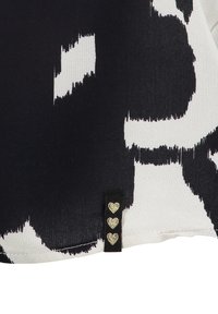 Zwart-wit gestreepte stof met abstracte vormen; voorzien van een zwart label met drie gouden hartaccenten nabij de zoom.