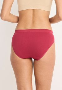 Mutande hipster rosse in cotone con una fascia larga in vita, texture liscia e dettagli di cucitura minimi, che mostrano una vestibilità aderente e una forma arrotondata.