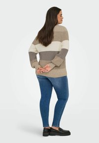 Beige and gray striped sweater with long sleeves, open back, and ribbed texture, paired with blue skinny jeans and black footwear.