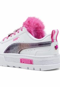 Bílá teniska Puma s třpytivým černým pruhem, růžovými tkaničkami, huňatým růžovým jazykem, růžovým logem, pruhovanou patní záložkou a růžovým kamínkem na patě.