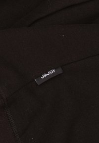 Zwarte stof met een zachte textuur, met een zichtbaar label waarop in witte letters op een zwarte achtergrond "J&Joy" staat.