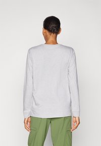 Hellgraues langärmliges Shirt mit Rundhalsausschnitt, aus weichem Stoff gefertigt. Schlichte Gestaltung mit leicht figurnahen Ärmeln, kombiniert mit grünen Cargo-Hosen.