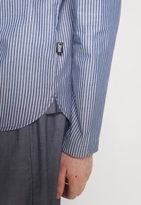 Blauw-wit gestreepte langemouwen shirt met een gebogen zoom en knoopmanchetten, met een klein zwart label nabij de zijnaad.