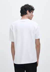 White cotton t-shirt with short sleeves, round neckline, and a relaxed fit. Smooth texture, no visible patterns or accents.