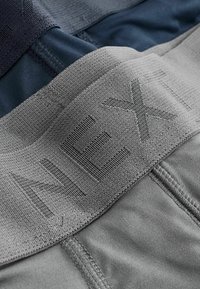 Primo piano di due slip boxer piegati, grigio e blu navy, che mostrano un elastico testurizzato con "AEXI" impressa sul paio grigio.