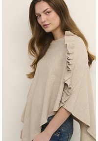 Smėlio spalvos didelio dydžio megztinis su raukinukais ant vienos peties. Minkšta, tekstūruota medžiaga, laisvo kirpimo, derinama su džinsais.