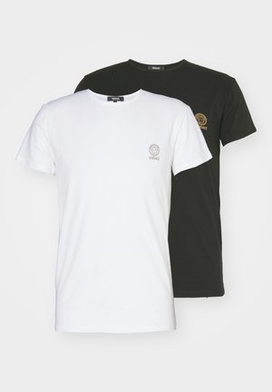Duas t-shirts de decote redondo: uma branca com um pequeno logótipo dourado e uma preta com um pequeno logótipo dourado. Ambas são feitas de tecido de algodão e têm mangas curtas.