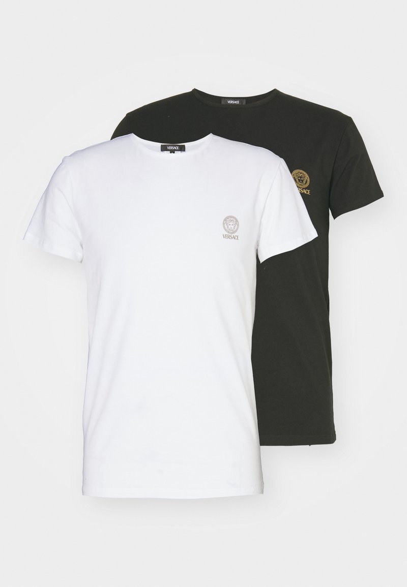 Two crew-neck T-shirts: one white with a small gold logo, one black with a small gold logo. Both are cotton fabric, short sleeves.