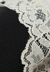 Zwarte ribstof met een witte kanten rand met bloempatronen. De kant heeft een delicate textuur met golvende randen.