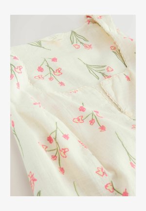 Hvid hørkjole uden ærmer med pink blomsterprint og bølget udskæring ved halsen.