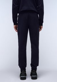 Donkerblauwe sweatpants van zachte stof, met ribbels aan de broekspijpen en een relaxte pasvorm. Draag ze met zwarte wandelschoenen met grijze accenten.