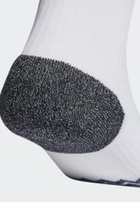 Chaussette blanche avec un talon noir texturé, présentant un mélange de motifs lisses et côtelés. Zone de talon renforcée pour plus de durabilité.