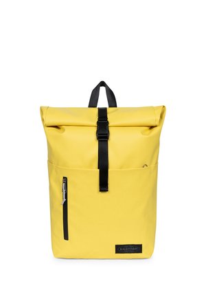 Sac à dos jaune à rabat roulé avec sangle à boucle noire, poche zippée à l'avant, poignée de transport et logo Eastpak dans le coin inférieur droit avant.
