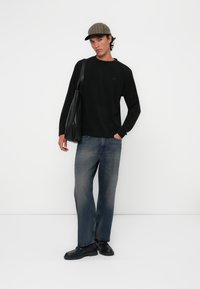 Svart langermet skjorte, blå jeans, svarte sko og en rutete caps. Modellen holder en svart tote-bag. Enkelt, uformelt design.