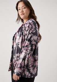 Blommönstrad cardigan i rosa och svart, tillverkad av textil med struktur. Öppen front med avslappnad passform och långa ärmar.