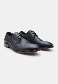 Scarpe eleganti in pelle nera con design perforato, punta tonda, lacci piatti e suola marrone. Presentano sezioni lisce e testurizzate.