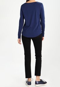 Tummansininen pitkähihaisen paita pyöreällä kaula-aukolla, yhdistettynä mustiin kapeisiin housuihin ja tekstuuripintaisiin sinisiin kenkiin.