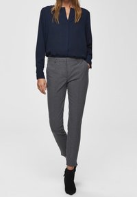 Mörkblå blus med v-ringning och långa ärmar, kombinerad med grå skräddarsydda byxor. Svarta ankelstövlar fulländar outfiten.