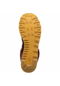 Semelle de chaussure de sport rouge et marron avec des crampons profonds et robustes ; matériau en caoutchouc jaune ; surface texturée avec détails du logo de la marque.