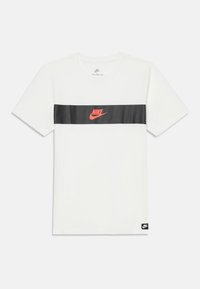 Bílý krátký rukáv Nike tričko s vodorovným černým pruhem přes hruď, na kterém je červené logo Nike a malá černá cedulka Nike na lemu.