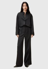 Camicia di satin nera con colletto e bottoni, abbinata a pantaloni ampi coordinati. Caratteristiche includono una texture liscia e un design su misura.