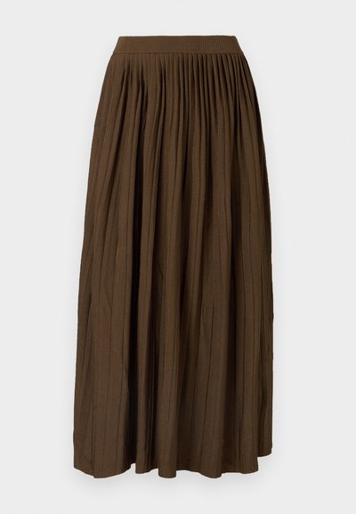 Brahmā pleitota maksi svārku ar platu elastīgu jostu un teksturētu audumu, kurā ir vertikāli salocījumi, lai pievienotu detaļas un plūsmu.